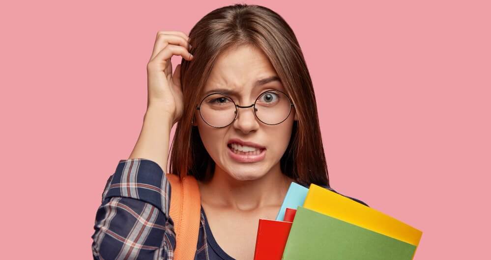aluno-intrigado-e-inseguro-posando-contra-a-parede-rosa-com-oculos (1)1 (1)